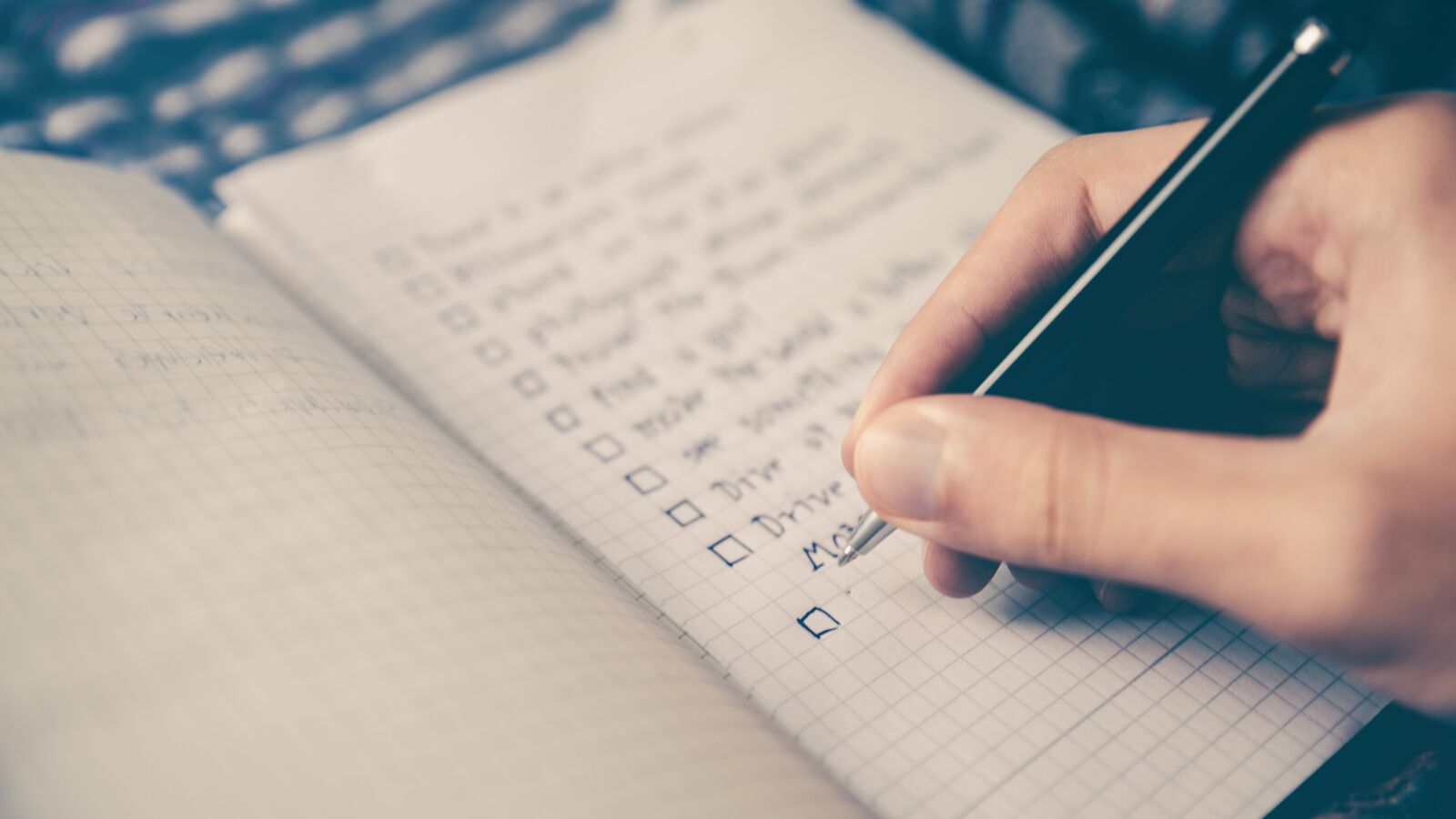 A hand ticking off a checklist in a notebook with a pen