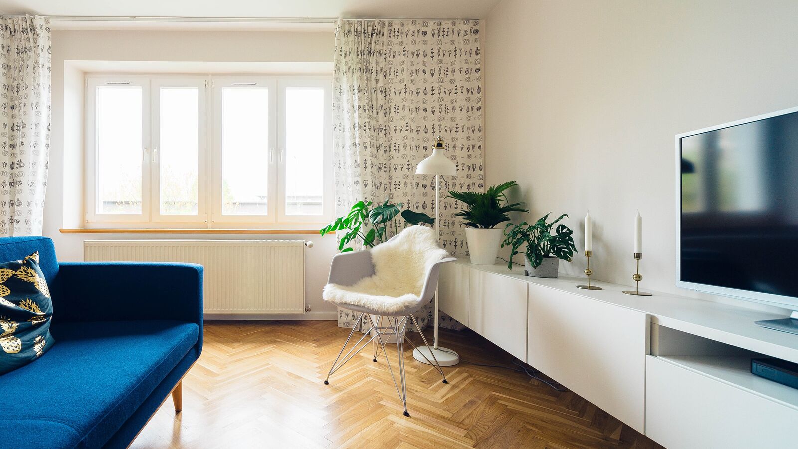 A bright living room with a blue sofa, an armchair and a flat-screen television on a white media console