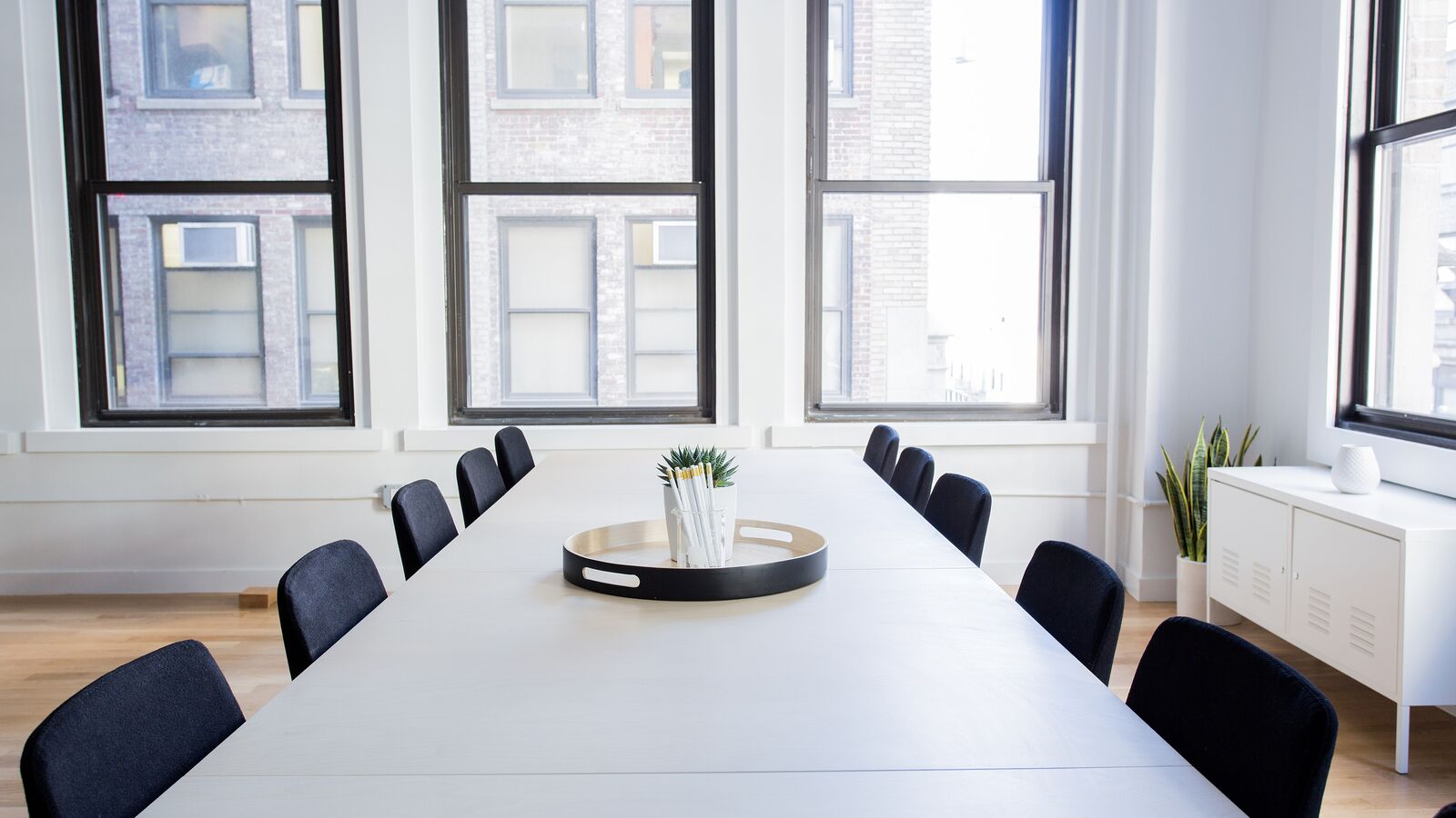A bright meeting room with a long white table, dark chairs and large windows