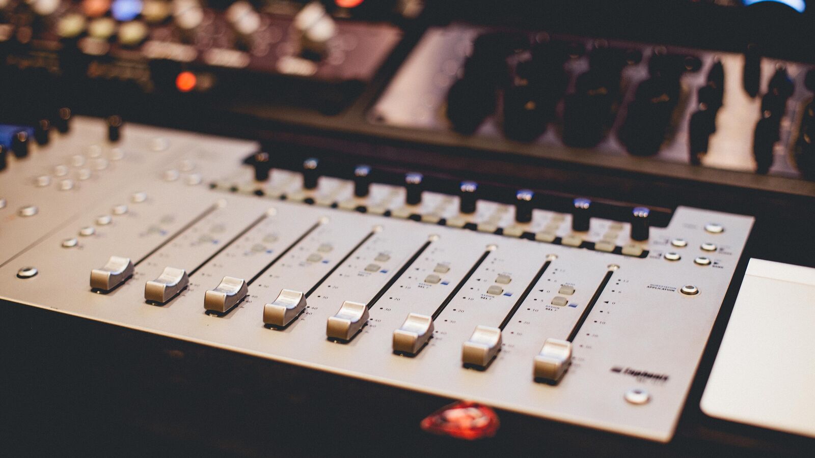 Close-up of a silver audio mixing console with a row of faders