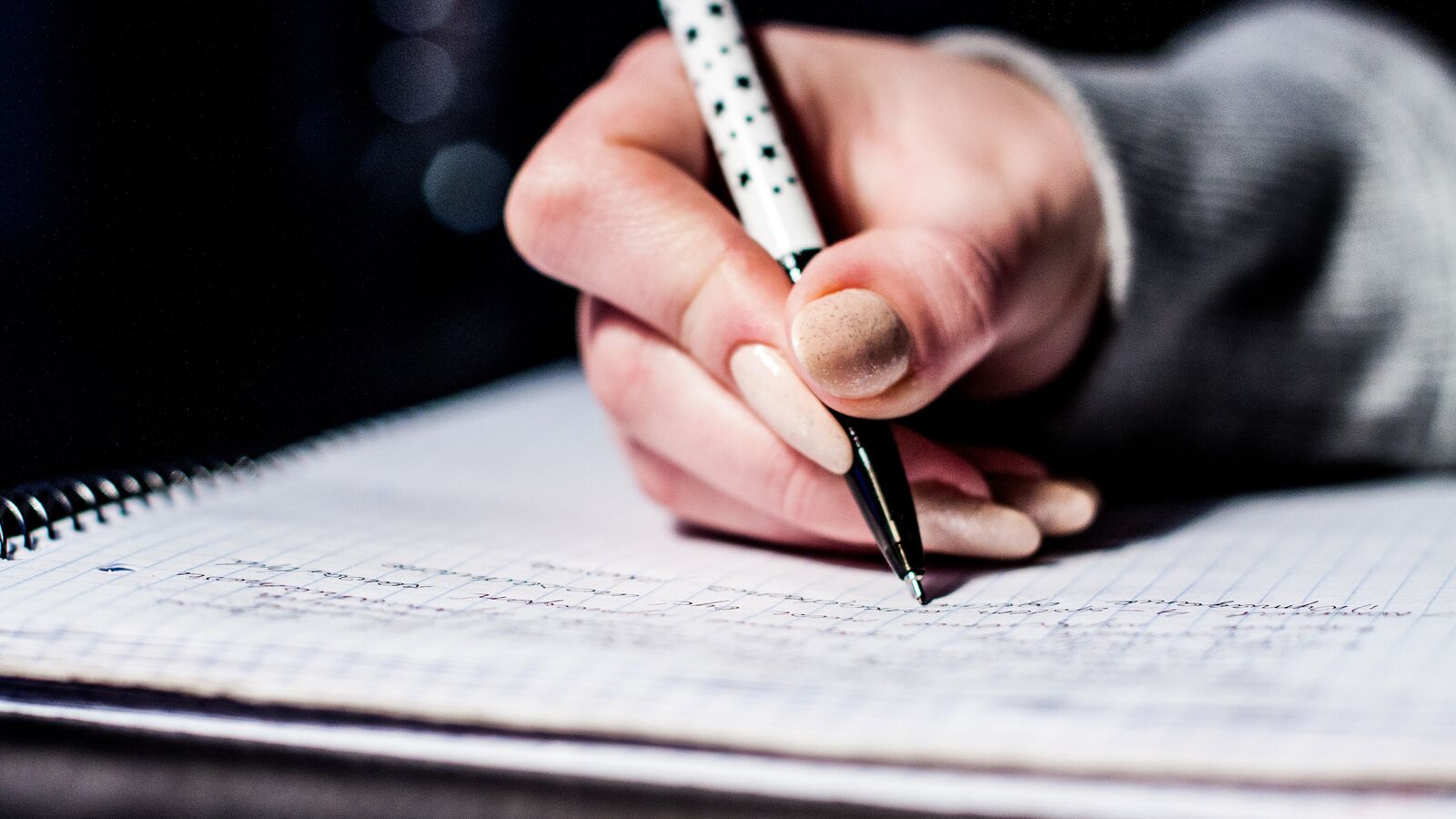 A hand writing in a spiral notebook with a dotted pen